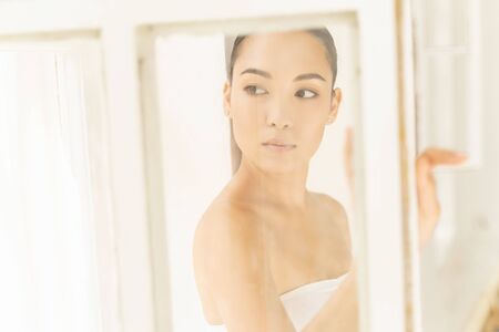 Concentrated Asian sexy girl standing near window. Personal care conceptの写真素材
