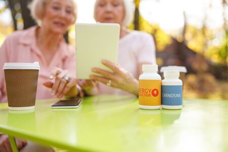 Close-up picture of two bottles with medicine standing on the table in front of two womenの写真素材