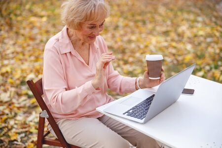 Cheerful aged lady typing on her laptop sittng in the street cafe