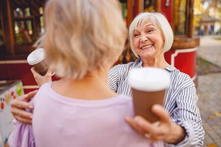 Cheerful aged lady with a cup of coffee going to hug her mateの写真素材