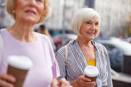 Two enthusiastic aged ladies walking and drinking coffeeの写真素材