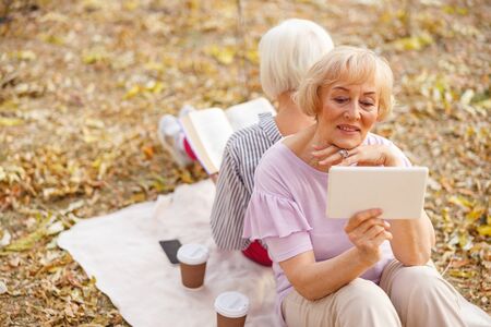 Two relaxed aged women sitting on a blanket and enjoying their books