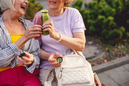 Cheerful aged ladies sitting on a bench clanging their smoothie bottlesの写真素材