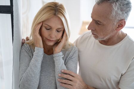 Woman having headache and touching her temples while standing next to her husband