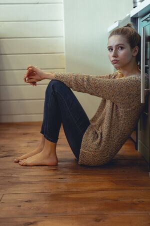 Alone at home. Negative delighted female leaning on furniture while sitting on the floor