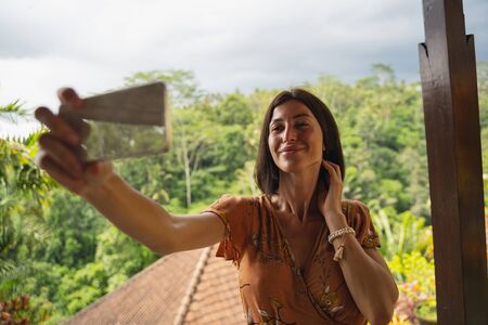 Attractive female person keeping smile on her face, looking at screen of her mobile telephoneの写真素材