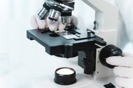 Modern laboratory. Close up of male hands in gloves that putting sample of reagent to check with help of microscopeの写真素材