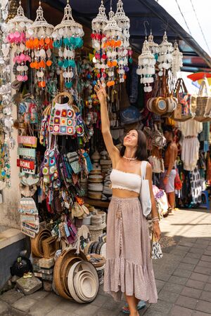 Cheerful young lady is walking in local streets between souvenir shops with handmade charms during her tripの写真素材