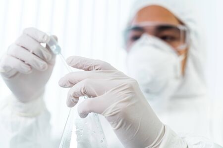 International researcher. Attentive Asian scientist using protective mask while working with...