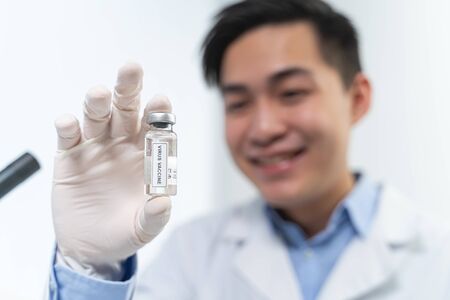 Pleased Asian medical worker expressing positivity while showing antiviral vaccine, working in...