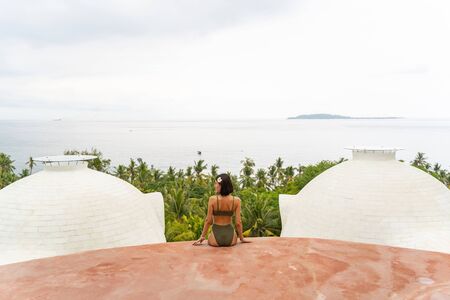 Back view of a modern young Caucasian female tourist sitting on a stone terrace outsideの写真素材