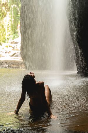 Enjoy the moment. Kind young woman wearing swimsuit while having stop near waterfall during excursionの写真素材