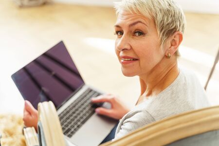 Portrait of a pleased beautiful senior Caucasian lady with her laptop smiling at the camera