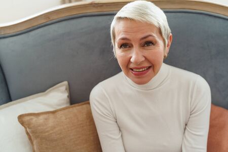 Waist-up portrait of a pleased lovely aged lady in a sweater smiling at the camera