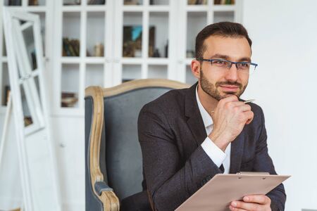 Waist-up portrait of a smiling male with a pen in his hand looking into the distanceの写真素材