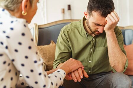 Senior female psychotherapist rendering professional assistance to a suffering young man during the...