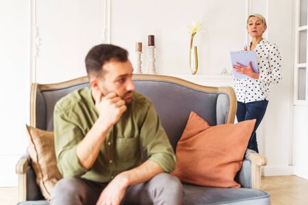 Senior focused female psychoanalyst with a clipboard in her hand standing behind her male patientの写真素材