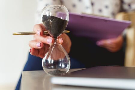 Cropped photo of a female psychotherapist putting an hour glass on a desk in her officeの写真素材