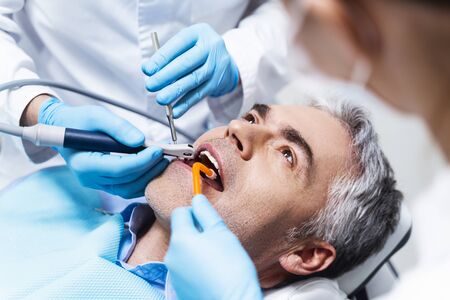Male is lying in dental chair and being given root canal by dentist and assistantの写真素材