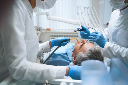 Dental specialist and nurse are helping man with teeth problems and giving him filling in clinicの写真素材
