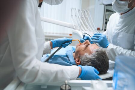 Dentist and his assistant are treating man in dental chair and giving him root canalの写真素材