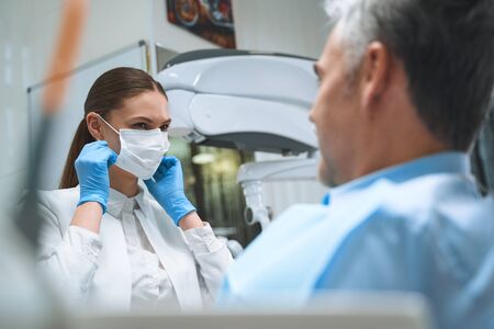 Merry woman in sterile mask and gloves is treating man in chair during his visit to dental clinicの写真素材
