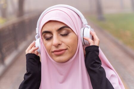 Portrait of a calm beautiful Muslim woman closing her eyes and listening to music in headphonesの写真素材