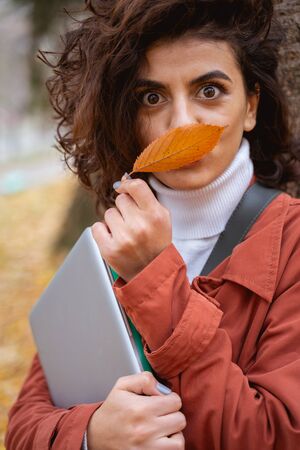 Pretty woman with laptop making funny faces and putting a leaf in front of her mouth