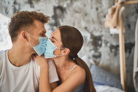 Loving couple. Pleased male person keeping eyes closed while trying to kiss his partner. Care...