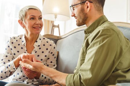 Smiling Caucasian aged professional female palm reader looking at a handsome short-haired young male clientの写真素材