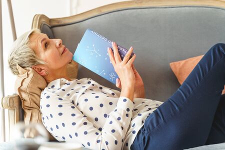 Side view of a smiling beautiful dreamy aged woman lying on a sofa at home