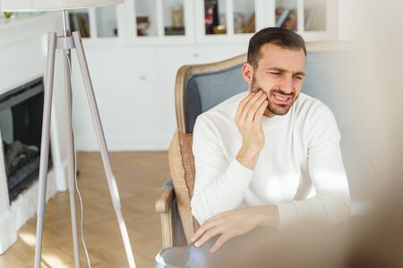 Front view of a dark-haired Caucasian male suffering from an acute dental pain at home