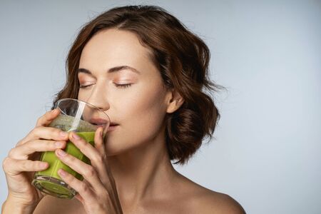 Happy beautiful female is drinking green freshly squeezed juice isolated on grey background stock photoの写真素材