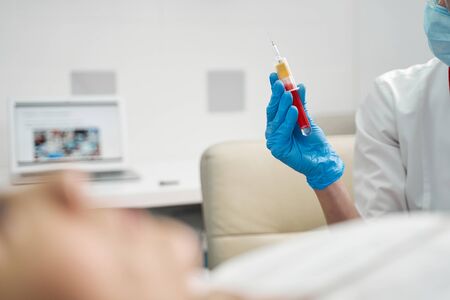 Concentrated young medical worker wearing protective mask while going to do blood analysisの写真素材