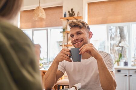 Sincere emotions. Handsome male person expressing positivity while spending morning in the kitchen, drinking teaの写真素材