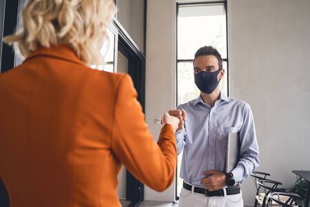 Fist bump. Dark-haired young Caucasian office worker greeting his blonde female colleague in the...