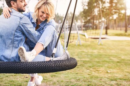 High-spirited beautiful young woman and her contented dark-haired boyfriend riding on a swing in the recreation zoneの写真素材