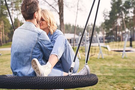 Pleased young Caucasian lady and her boyfriend sitting close to each other on a swingの写真素材