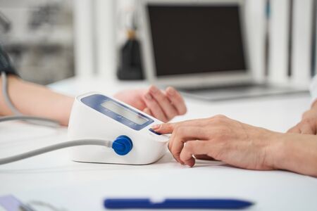 Professional medical worker sitting at the table while measuring blood pressure of her patient
