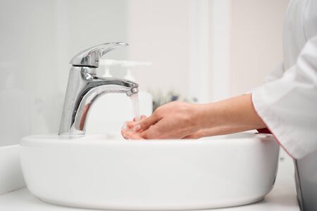 Focused photo on medical worker that standing in semi position near sink while making her hands sterileの写真素材