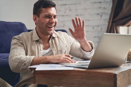 Closeup portrait of a high-spirited Caucasian remote worker sitting on the floor at his laptop