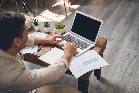 Back view of a dark-haired Caucasian male freelancer sitting at the computer online in his apartment