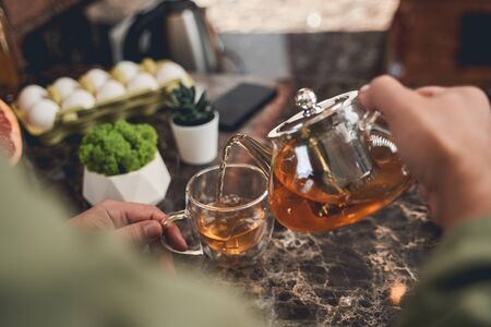 Cropped photo of a Caucasian man pouring a herbal beverage from a heat-resistant glass teapotの写真素材