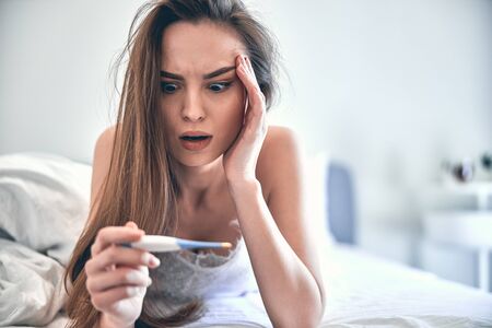 Young ill woman measuring temperature in bedroom at home stock photo. Lifestyle concept