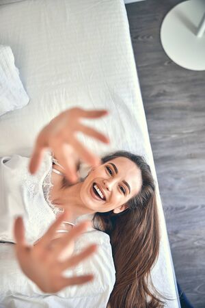 Caucasian cheerful girl laughing in light bedroom and pulling her hands to camera stock photo. Lifestyle conceptの写真素材