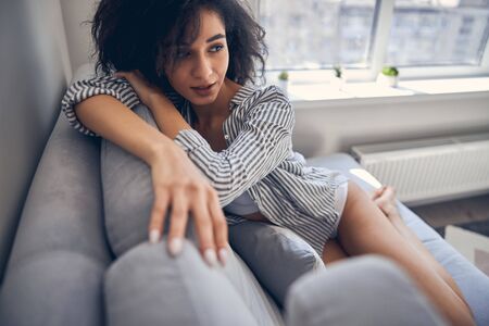 young lady with thick dark hair on the sofa staring into the distance