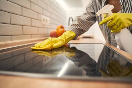 Busy housewife wearing rubber gloves while using cleaning agent, spending her morning active