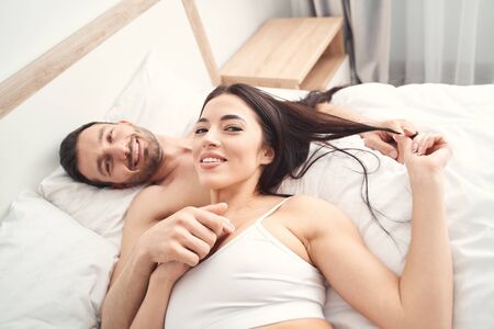 Top view of the pleased newlyweds posing in bed for the camera