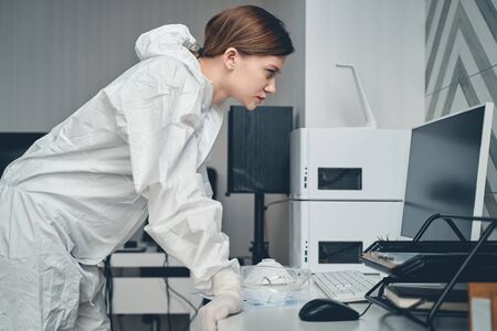Side view of serious pretty lady in safety suit working with desktop PC in modern office