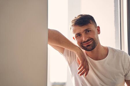 Close up photo of attractive brunette male giving a smile while leaning against the wallの写真素材